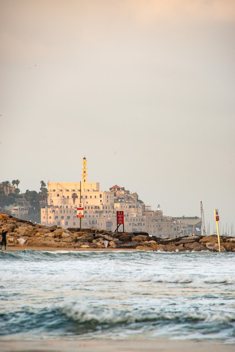 Ancient Jaffa old city skyline with mosque minaret glowing at golden hour viewed from Tel Aviv beach shoreline