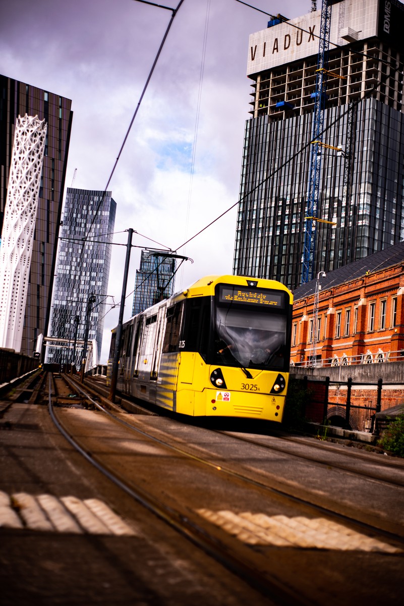 Yellow Metrolink tram 3025 passing through Manchester city centre with Viadux tower under construction in background